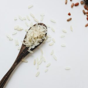 Top view of uncooked white and red rice grains in a wooden spoon on a white background, showcasing natural food.